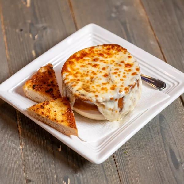 French onion soup with melted cheese and two pieces of toasted bread on a white plate.