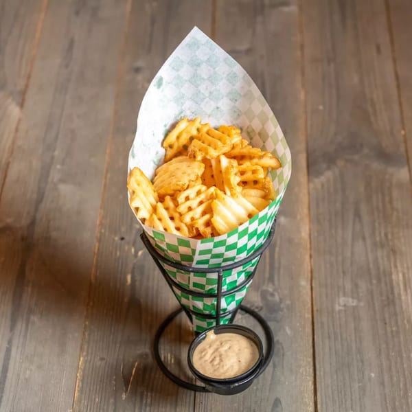 Crispy waffle fries in a green and white checkered paper cone, with a side of dipping sauce.