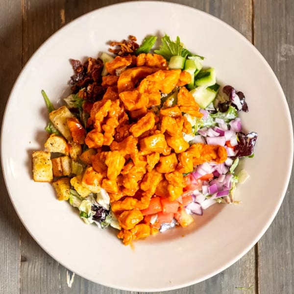 Overhead view of a salad with buffalo chicken, bacon, croutons, and mixed vegetables.