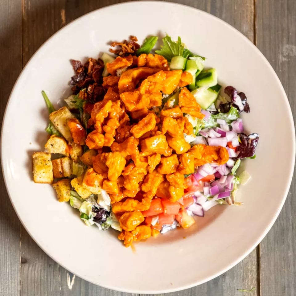 Overhead view of a salad with buffalo chicken, bacon, croutons, and mixed vegetables.
