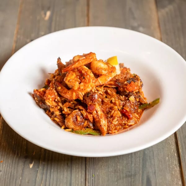 A white bowl filled with Cajun jambalaya, featuring shrimp, rice, and vegetables, on a wooden table.