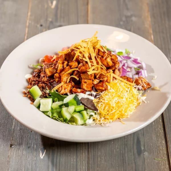 A large bowl of BBQ chicken salad with cheese, red onion, and tortilla strips.