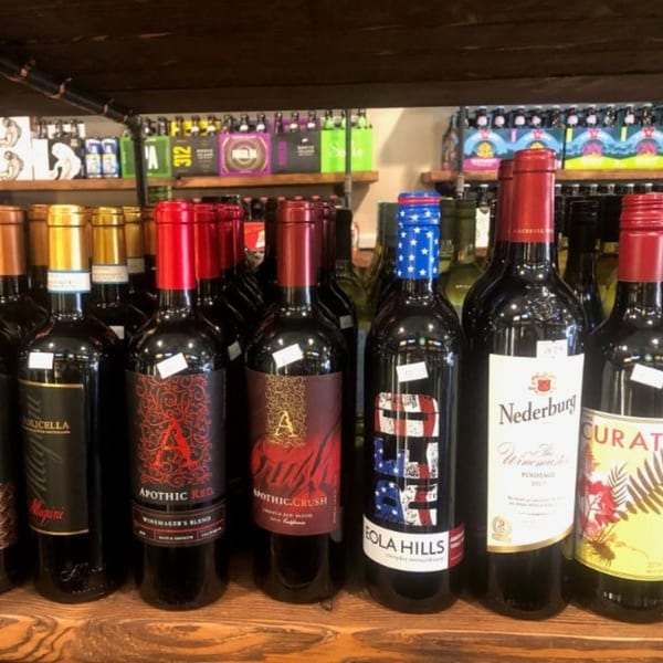A variety of red wine bottles with colorful labels displayed on a wooden shelf.