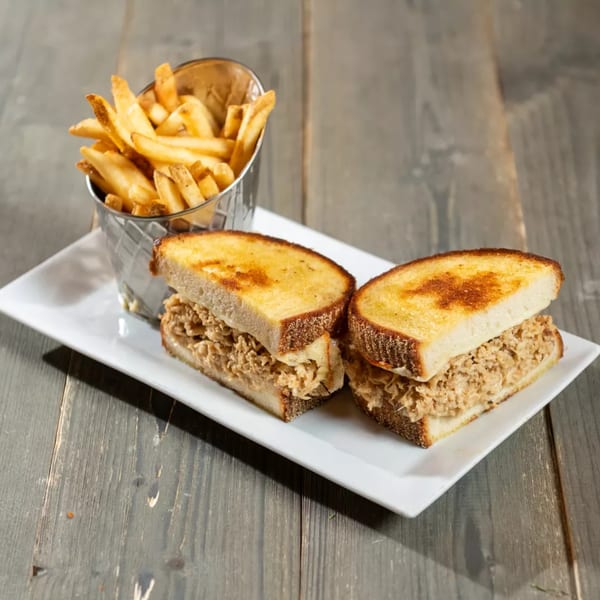 Two grilled sandwiches with shredded filling and a metal cup of french fries on a white plate.