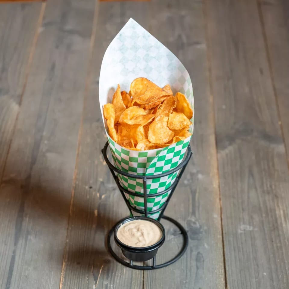 Crispy golden potato chips in a green and white checkered paper cone with a side of dipping sauce.