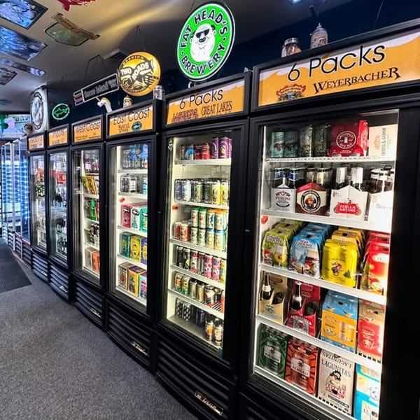 A row of refrigerated display cases filled with various beer and beverage six-packs.