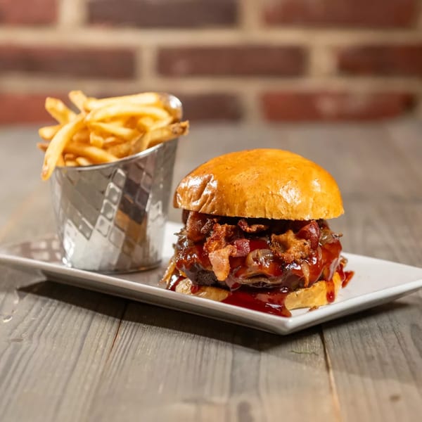Gourmet burger with bacon, caramelized onions, and BBQ sauce, served with a side of fries.