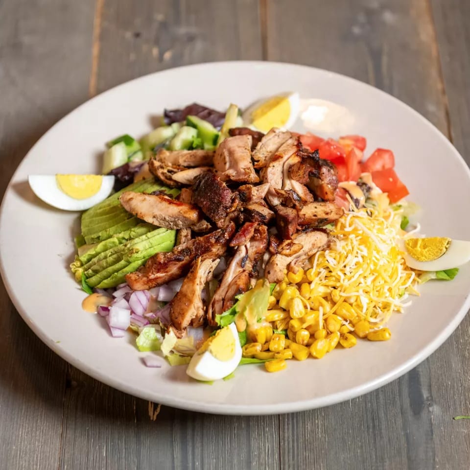 Grilled chicken salad with avocado, corn, tomatoes, cheese, red onion, and hard-boiled eggs.
