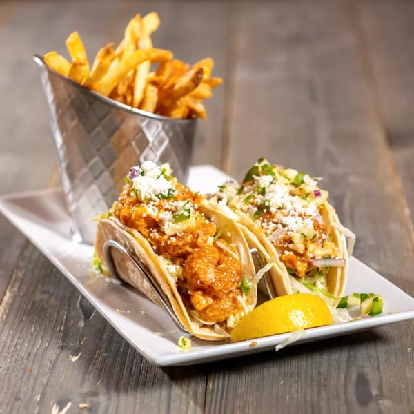 Two shrimp tacos with cheese and a side of french fries in a metal cup.