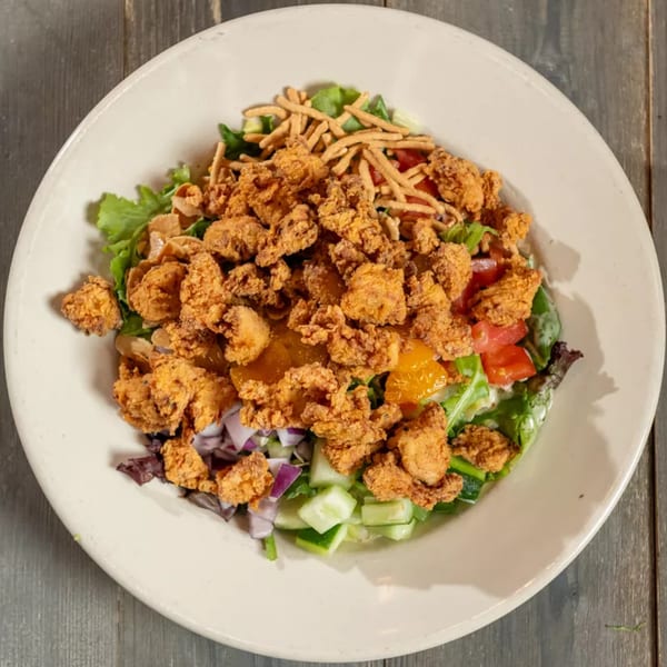Overhead view of a salad with fried popcorn shrimp, mixed greens, tomatoes, cucumbers, and red onions.