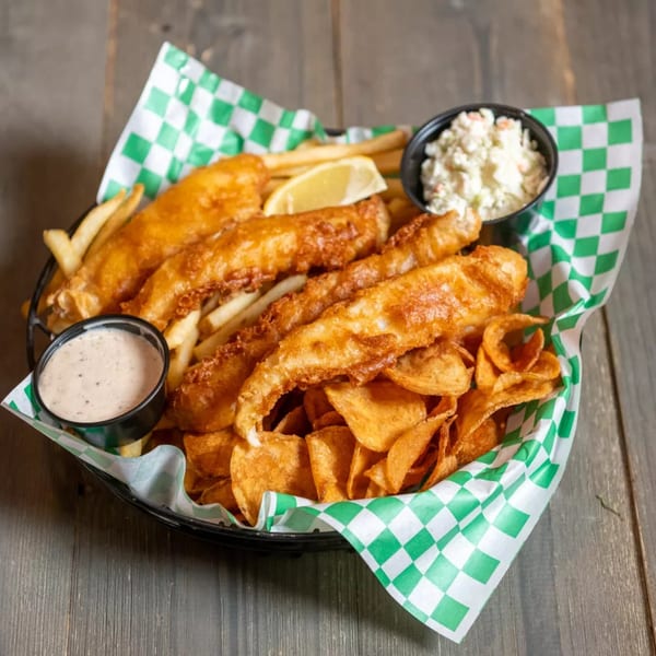 Crispy fish and chips with a lemon wedge, coleslaw, and tartar sauce in a basket.